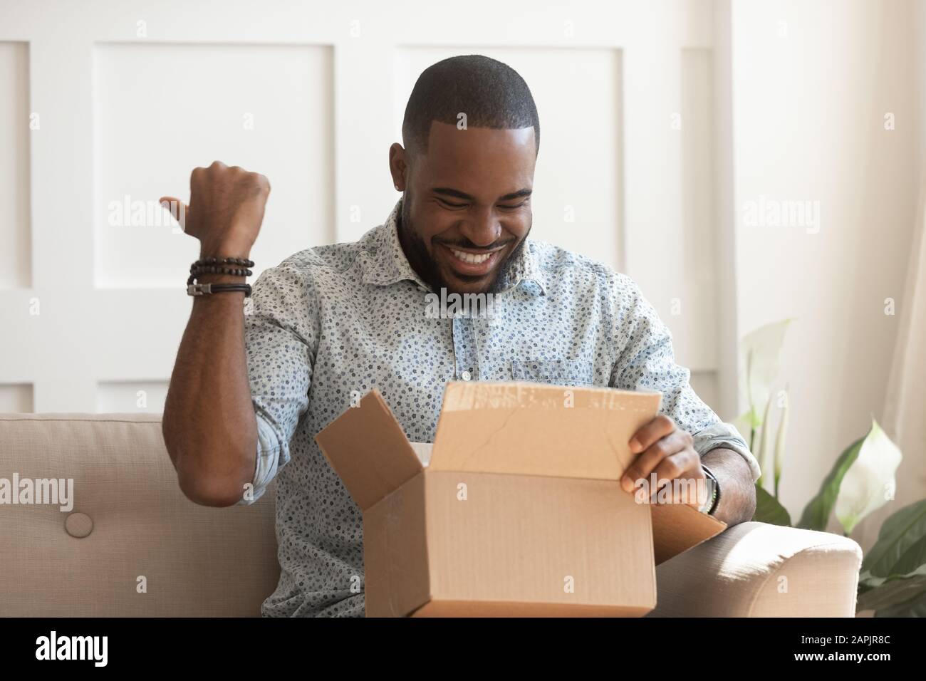 Happy african guy opening long-awaited parcel box Stock Photo