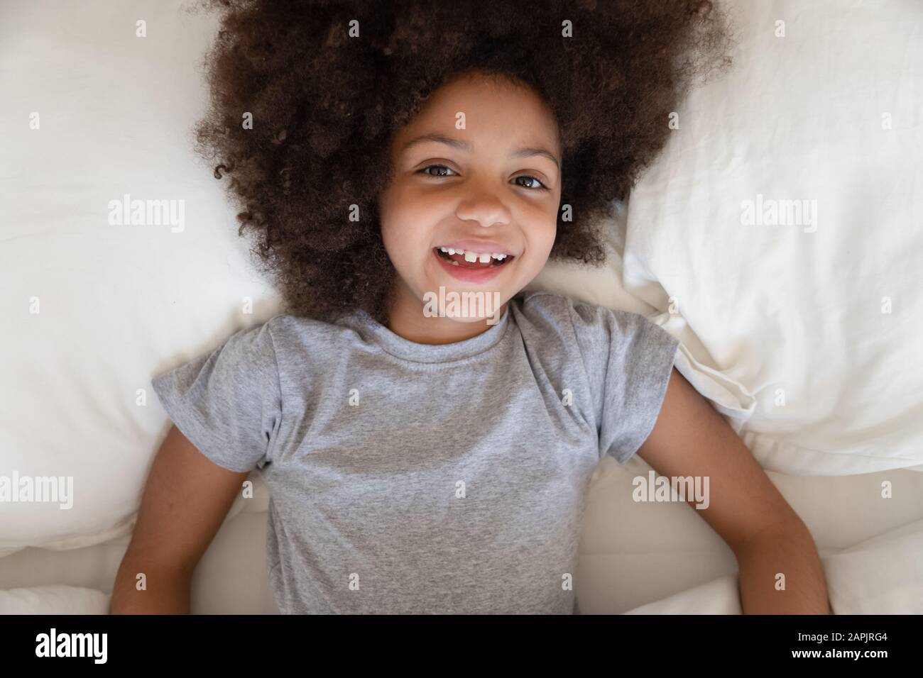 African little girl lies in bed smiles looking at camera Stock Photo