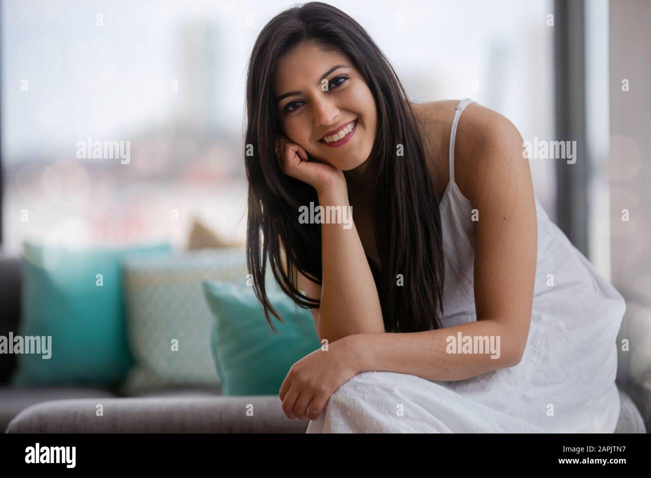 Cute adorable beautiful young Indian american woman at home sitting on sofa, smiling, cheerful, femininity, pretty face, portrait Stock Photo