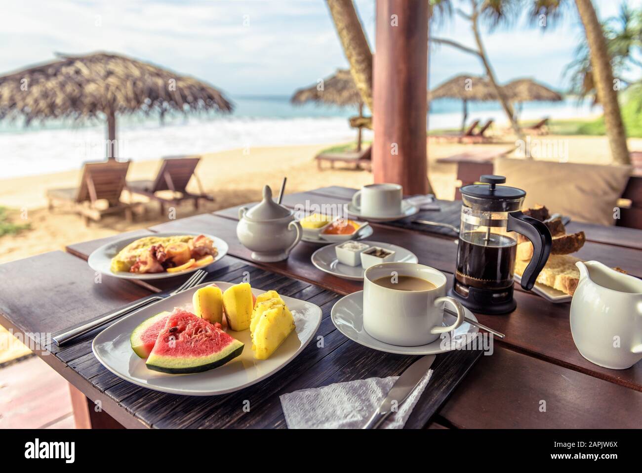 Breakfast on sea beach in Sri Lanka. Table setting with vegan food and coffee in restaurant outdoor. Buffet with exotic fruits on ocean coast. Concept Stock Photo