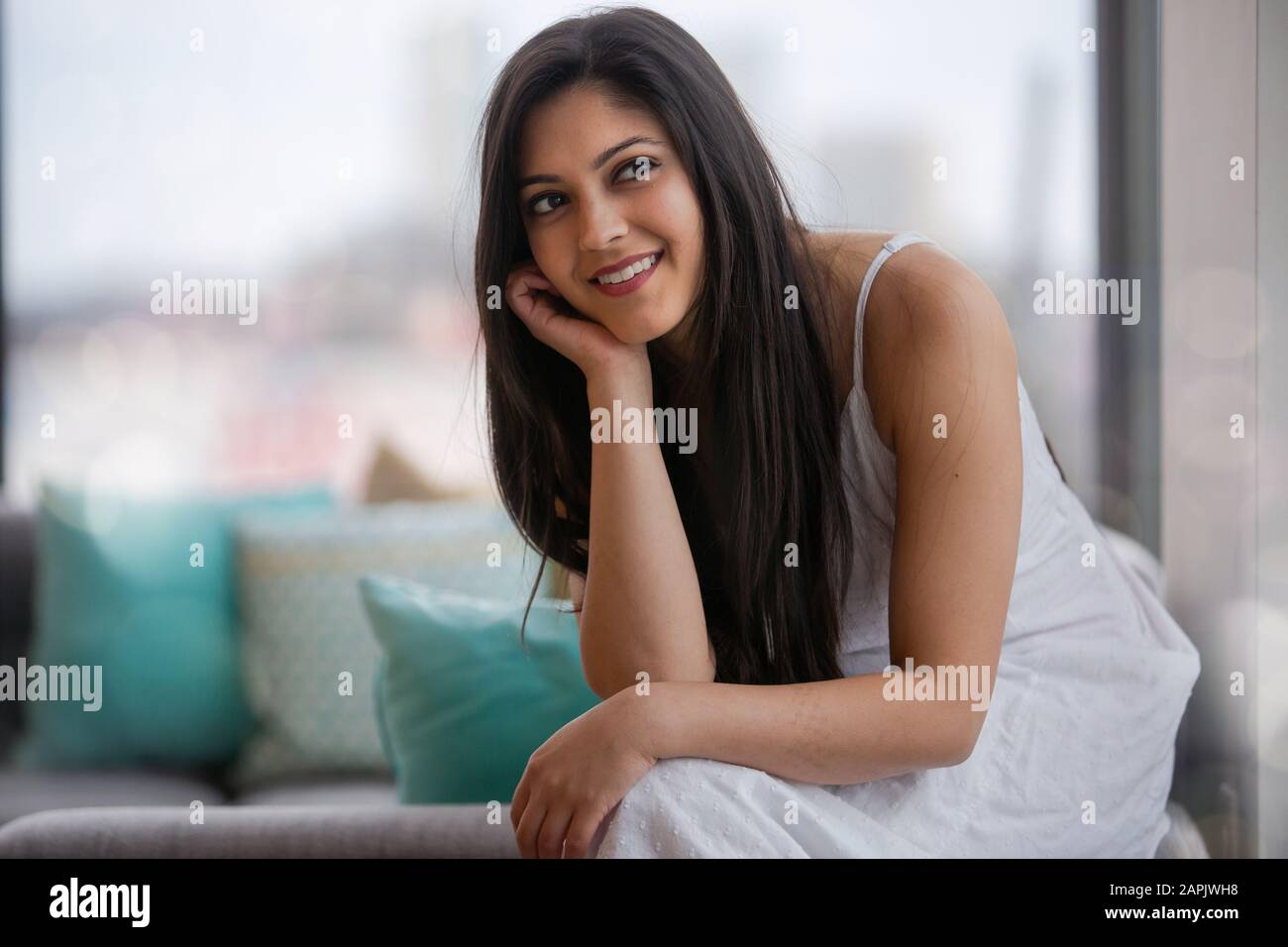 Adorable cute indian american, south asian multiracial mixed ethnicity woman in white dress, beautiful brunette and brown eyes, home lifestyle Stock Photo