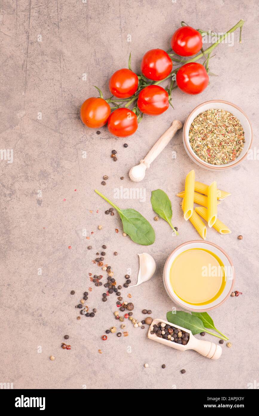 Pasta, tomatoes, italien spices, garlic, pepper corns and olive oil on a brown textured background Stock Photo
