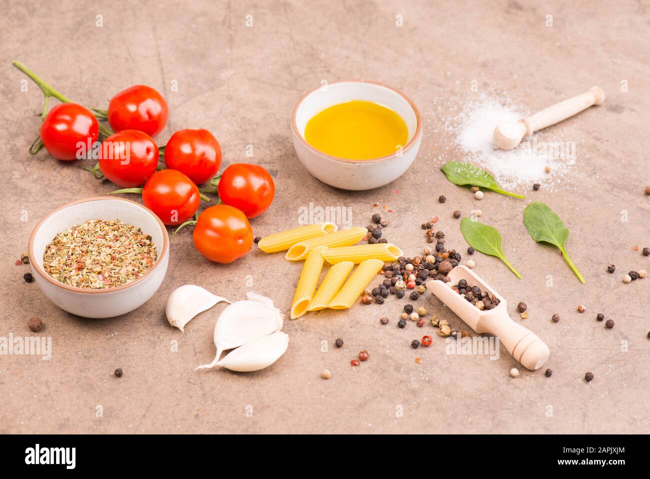 Pasta, tomatoes, italien spices, garlic, pepper corns and olive oil on a brown textured background Stock Photo