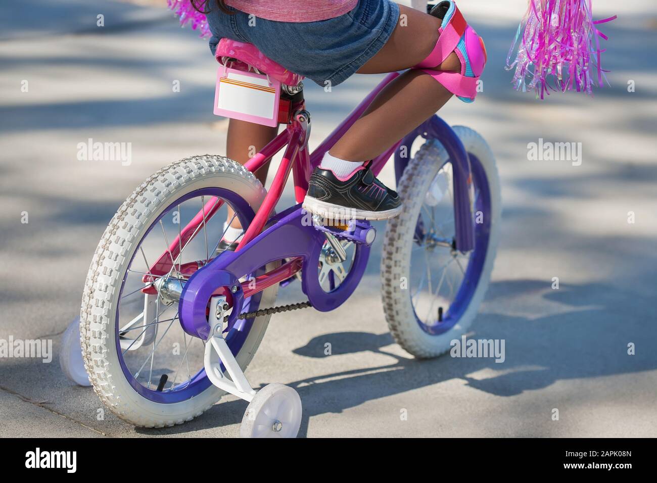 A little kid learning to ride a bicycle with training wheels and ready