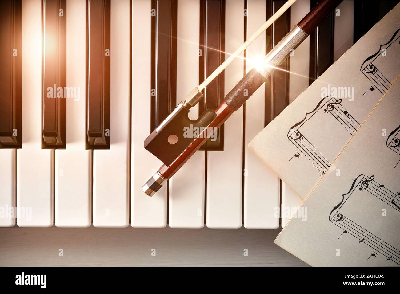 Bow with sheet music on piano keys top. Concept of interpretation of piano music and string instruments. Top view. Horizontal composition. Stock Photo