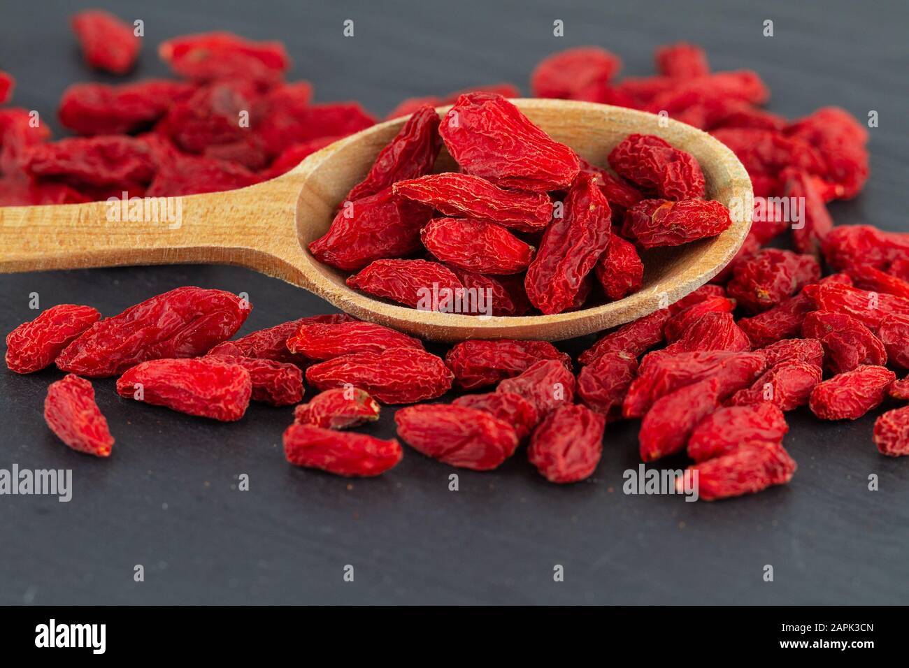 goji berries close up dried red berry in wooden spoon on grey slate plate Stock Photo
