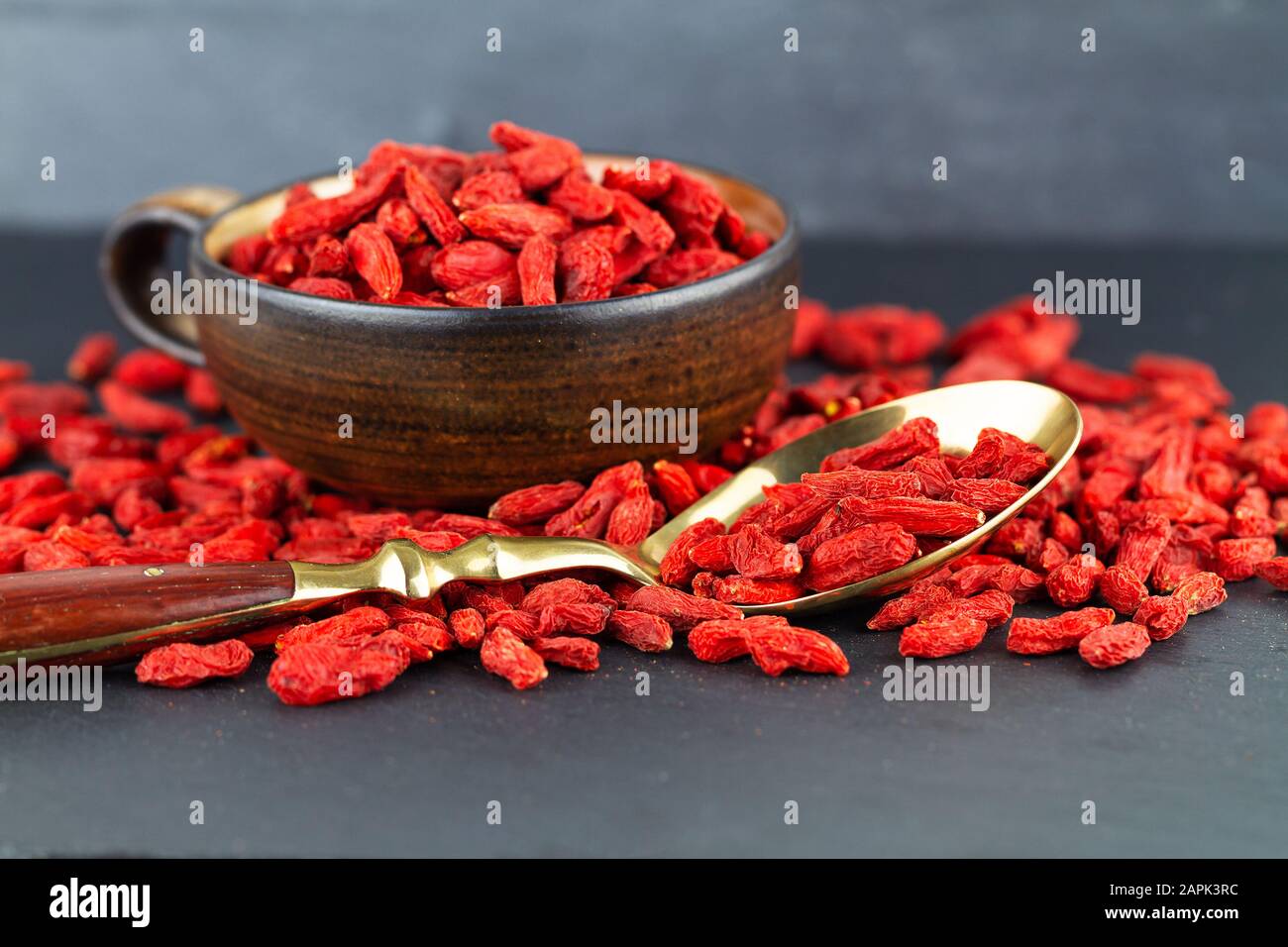 Goji berries in a cup and vintage spoon on gray slate background. Selective focus Stock Photo