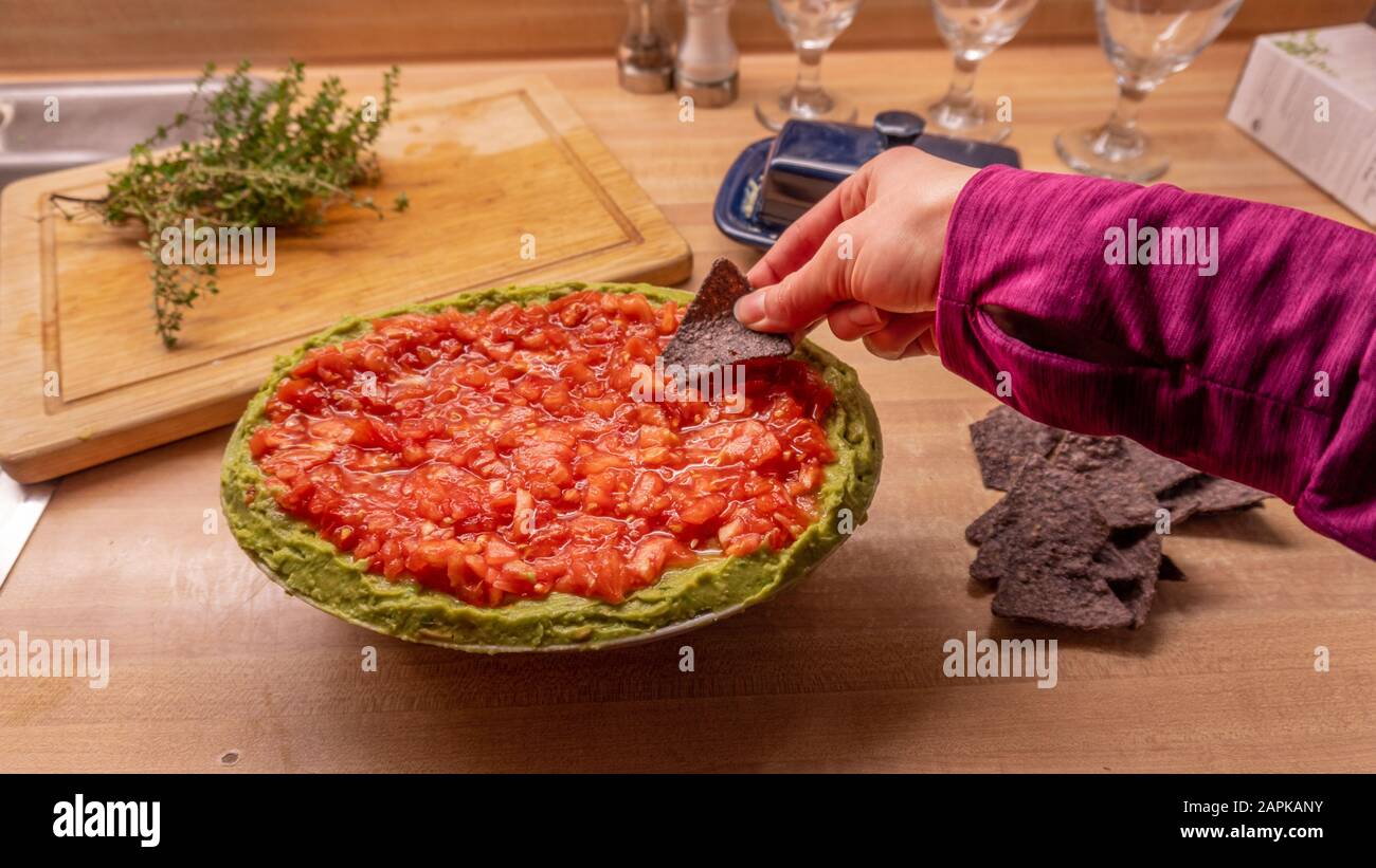 Casual girl dipping into Mexican salsa dip while holding nacho ...