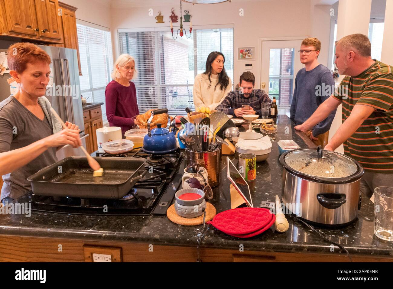 Family gathered around kitchen center island for buffet style Thanksgiving dinner Stock Photo