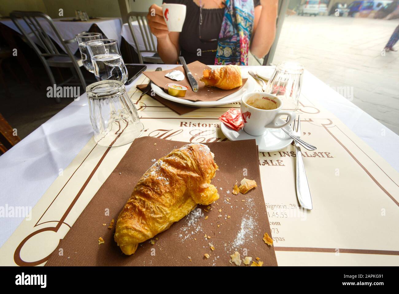 A half eaten croissant and breakfast at a sidewalk cafe as a couple enjoy breakfast in the Tuscan city of Florence, Italy Stock Photo