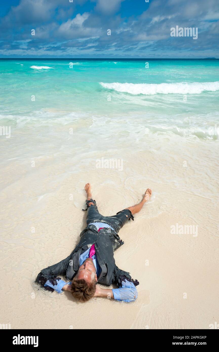 Castaway survivor businessman washed up on a tropical beach relaxing in a ragged torn suit Stock Photo