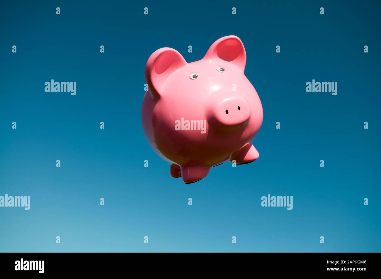 Wide-eyed pink piggy bank flying in clear blue sky copy space Stock Photo