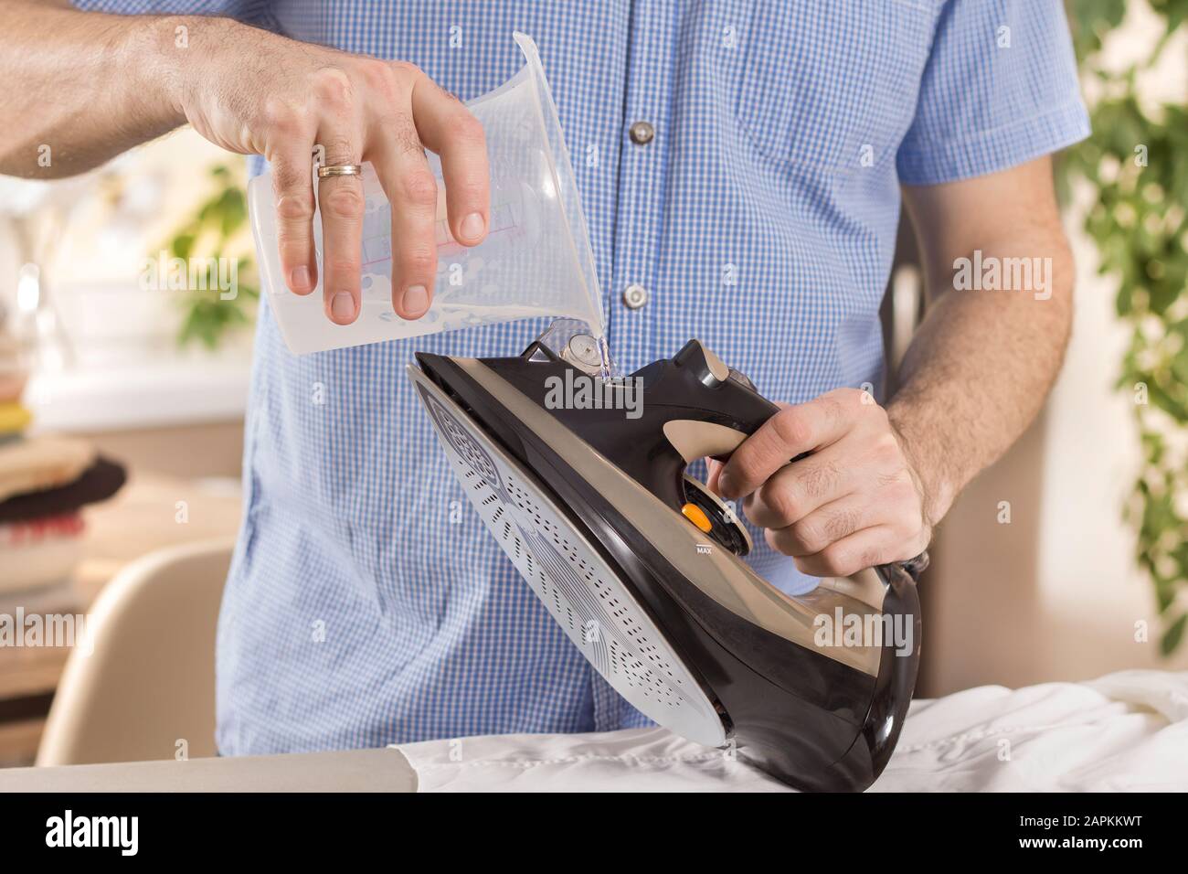Man in household duties. Ironing clothes. The man holds the iron in one  hand and in the other a container with water which he pours into the iron  Stock Photo - Alamy