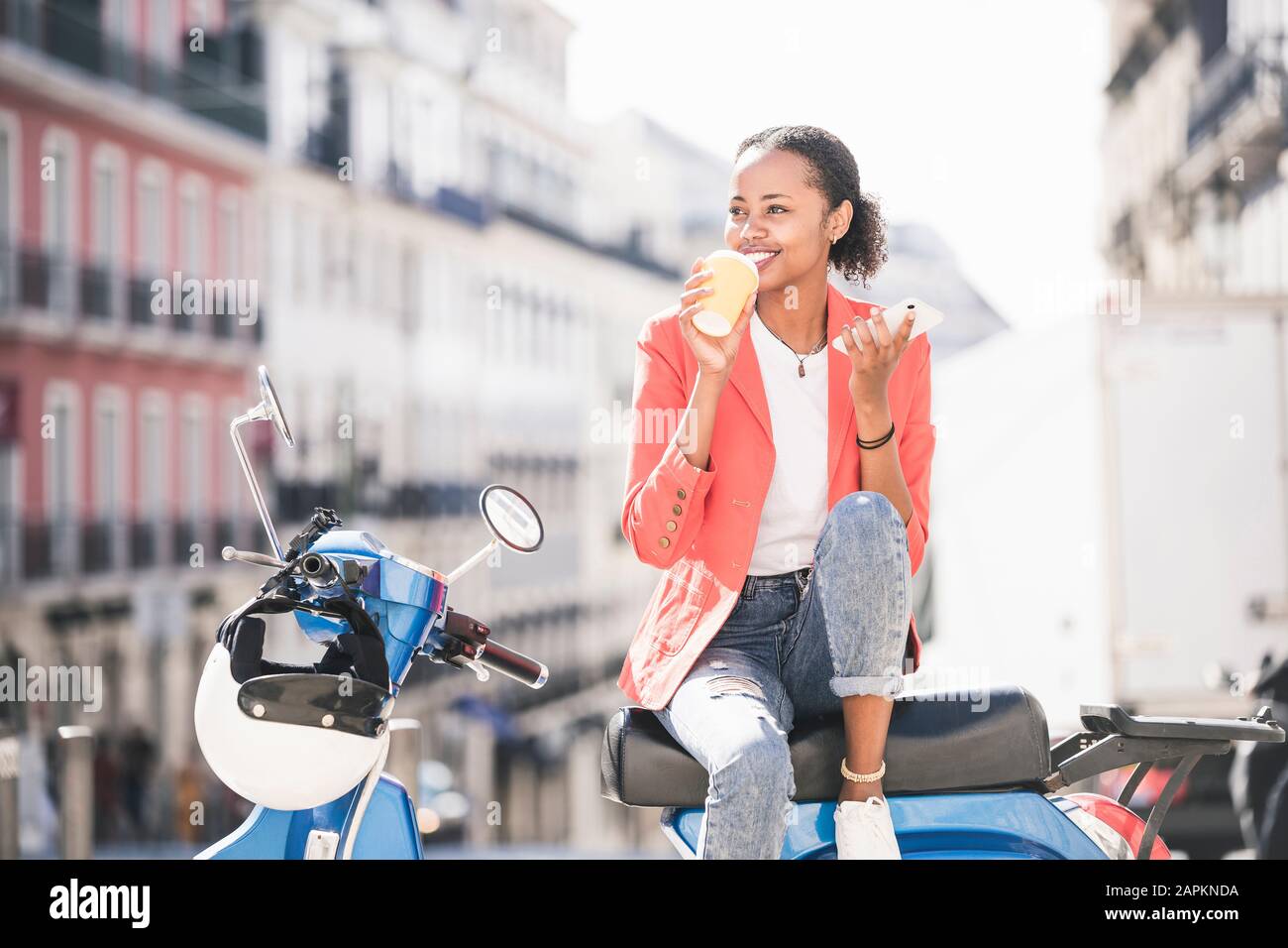 Smiling young woman with motor scooter drinking coffee in the city, Lisbon, Portugal Stock Photo