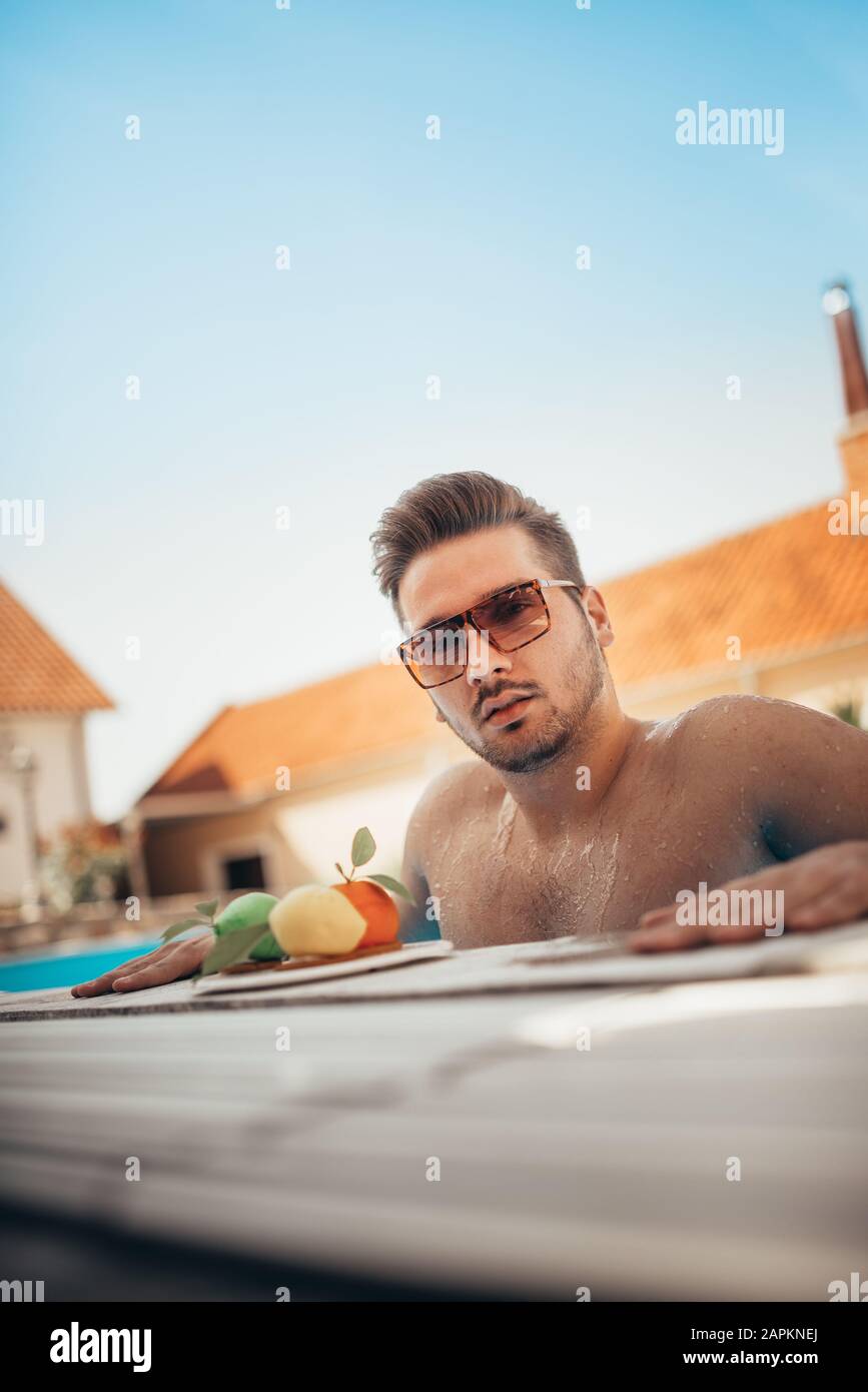 Young man in sunglasses resting on edge of swimming pool Stock Photo
