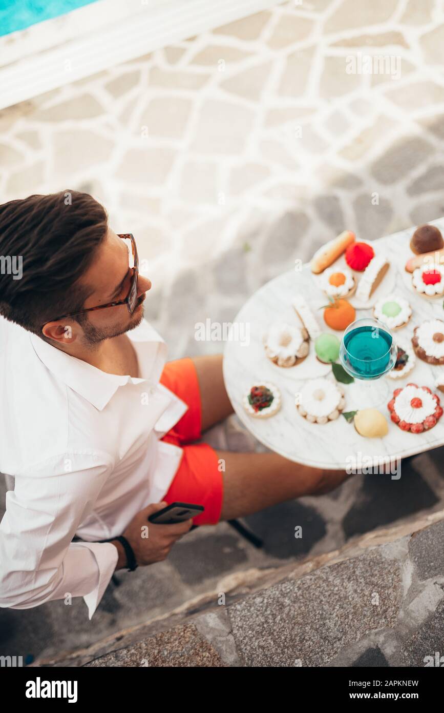 Handsome man sitting outdoors and drinking blue wine. Stock Photo