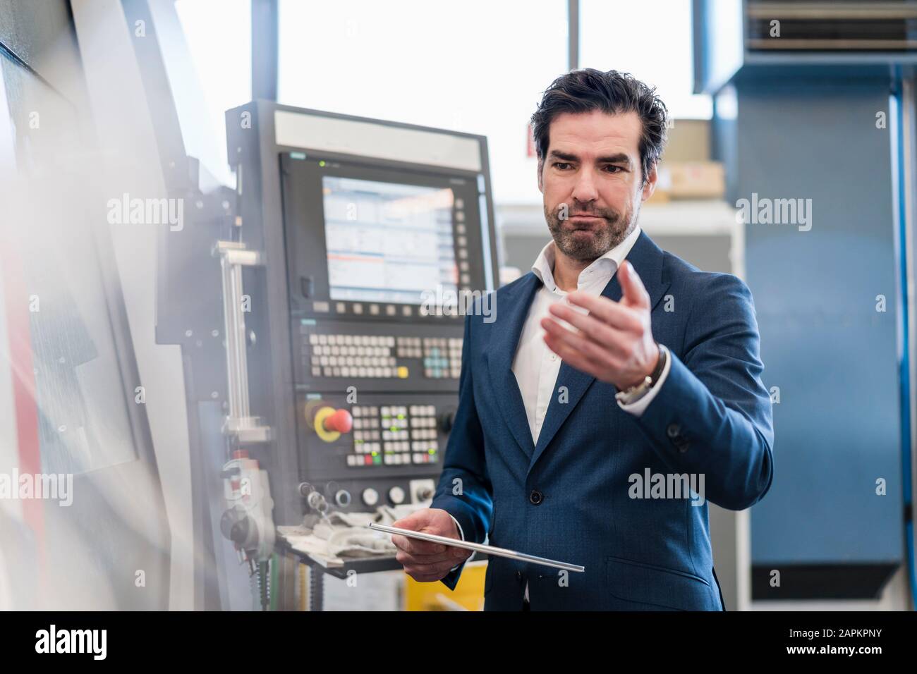 Businessman using tablet at a machine in a factory Stock Photo
