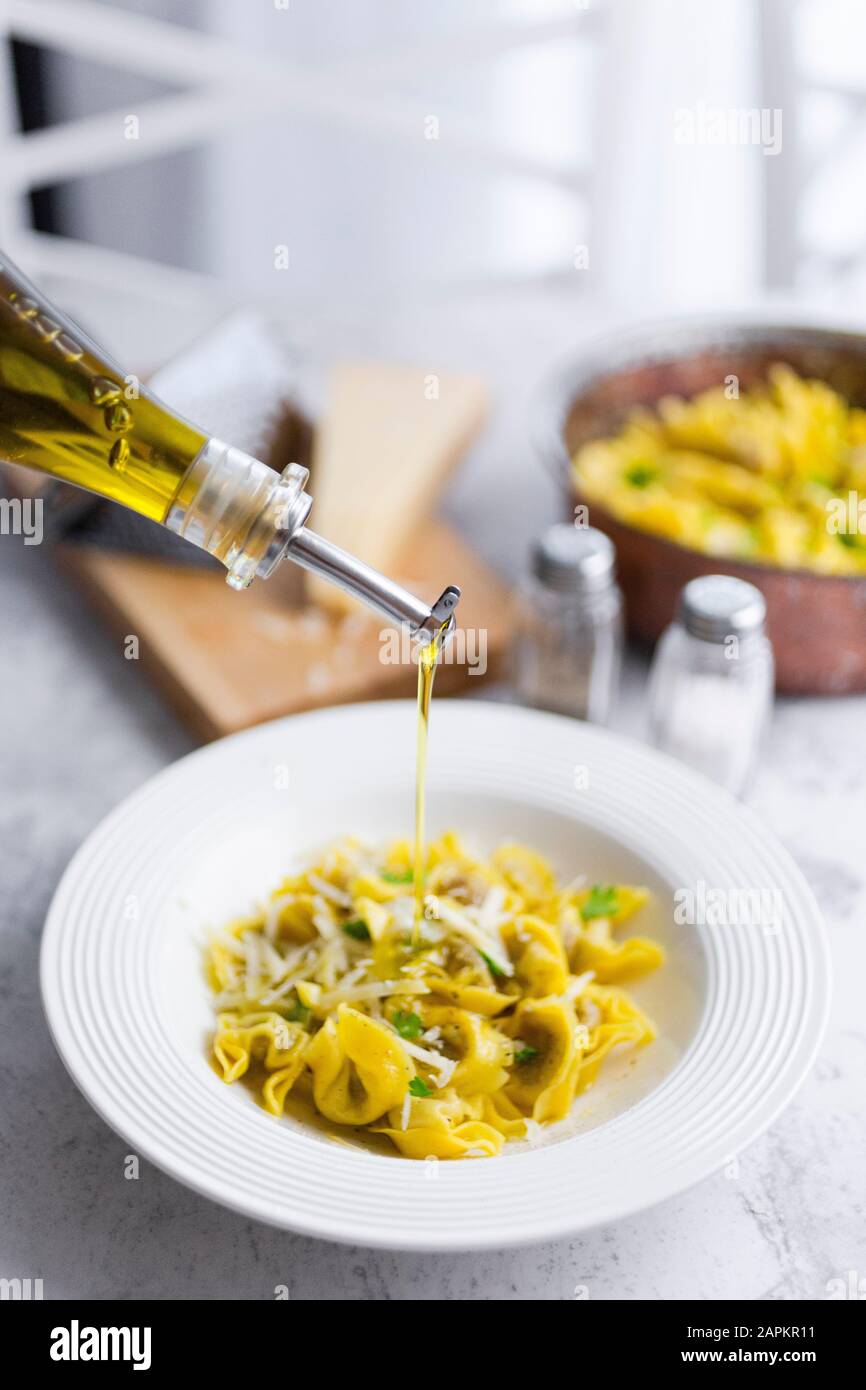 Olive oil pouring into plate of Italian tortellini with grana cheese Stock Photo