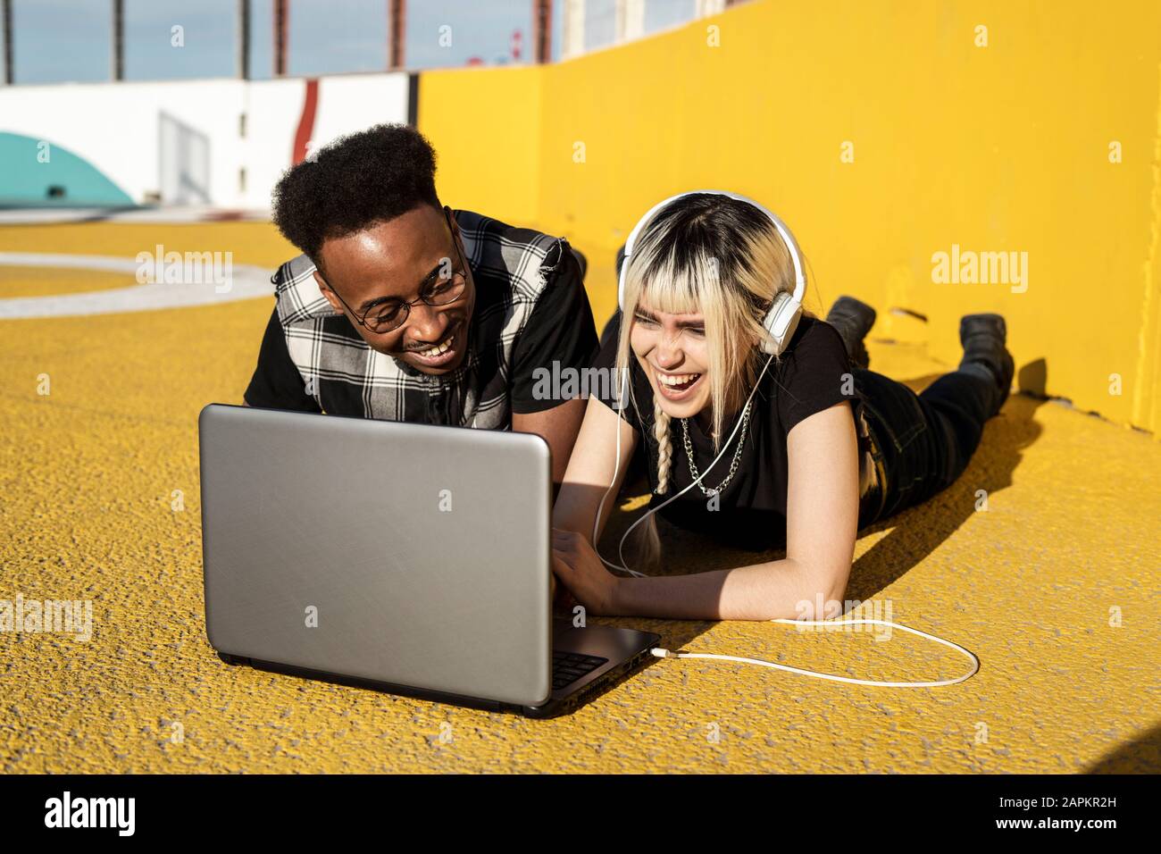 Laughing young couple using headphones and laptop outdoors having fun Stock Photo