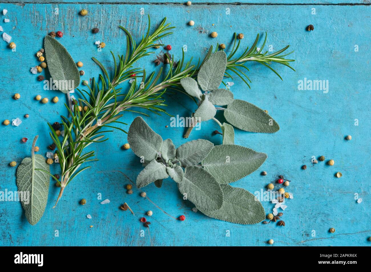 Rosemary, sage, salt and pepper lying on blue cutting board Stock Photo