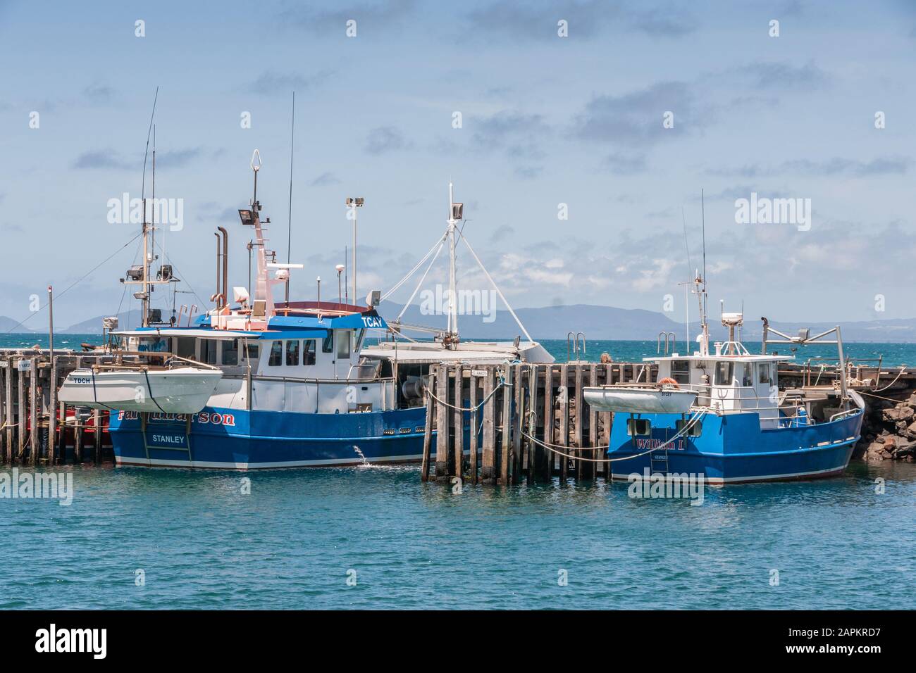 Stanley, Tasmania, Australia - December 15, 2009: Two white and blue fishing vessels docked at wooden pier of the port in azure water and under light Stock Photo