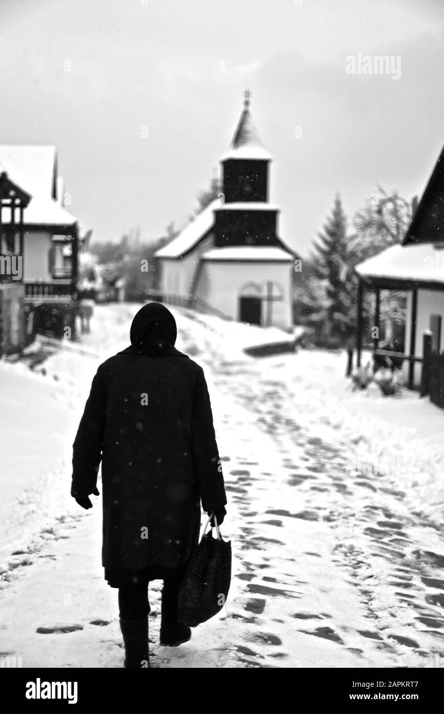 Grayscale shot of a man walking in hollókő village in hungary during winter Stock Photo