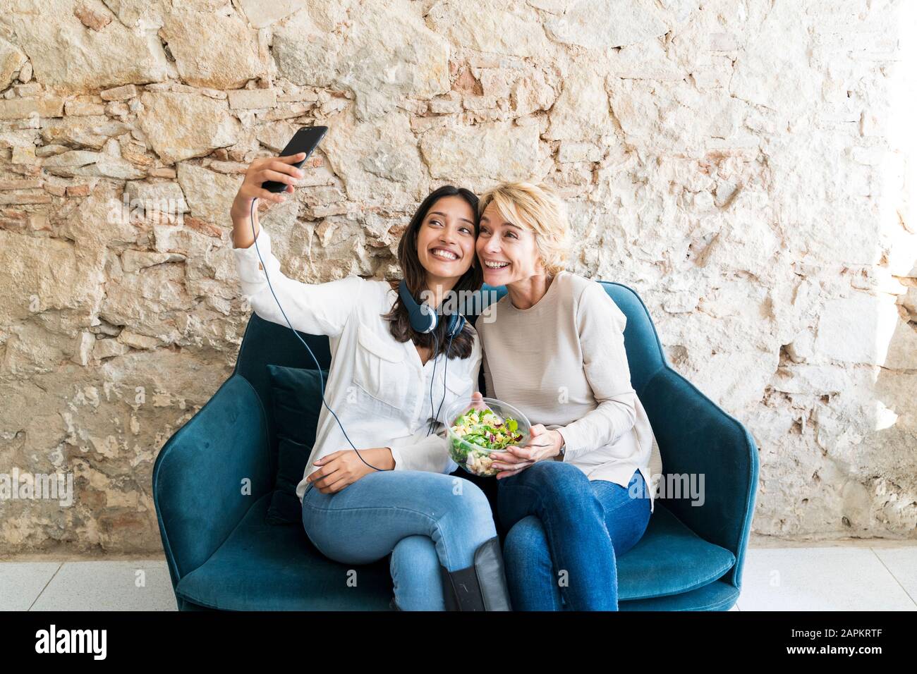 Two colleagues sitting on couch at lunchtime taking selfie with smartphone Stock Photo