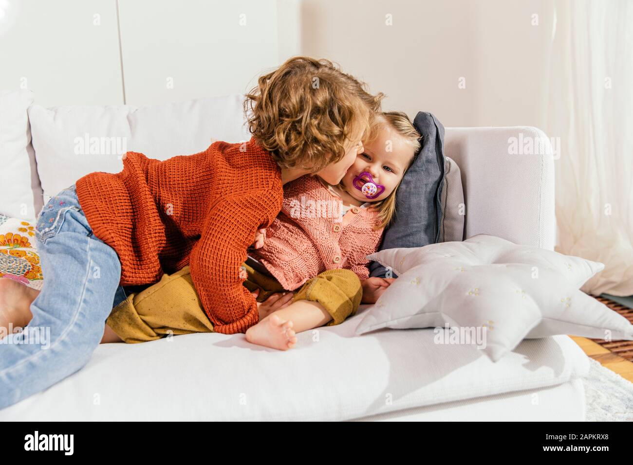 Two little sisters cuddling on couch at home Stock Photo