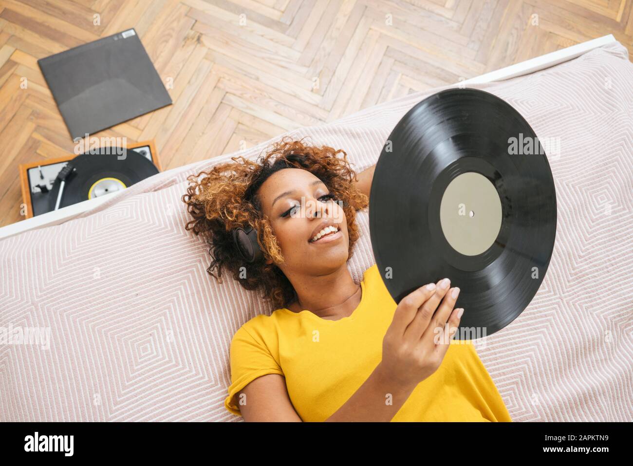 Young woman lying on bed listening to music with headphones and record player Stock Photo