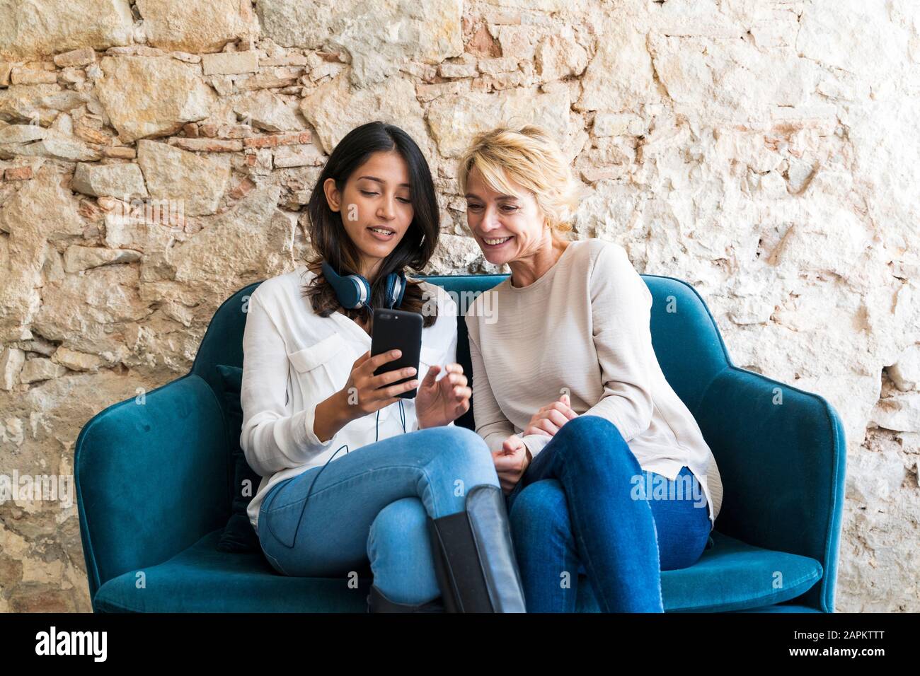 Portrait of two colleagues sitting on couch at looking at smartphone Stock Photo