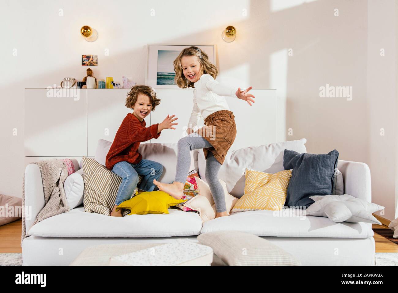 Two happy girls jumping on couch at home Stock Photo Alamy