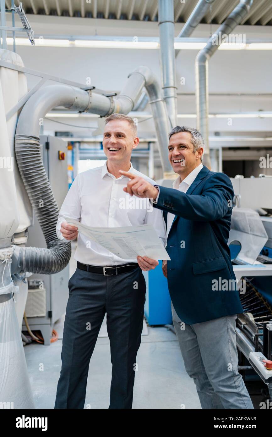 Two happy businessmen with paper talking in a factory Stock Photo - Alamy