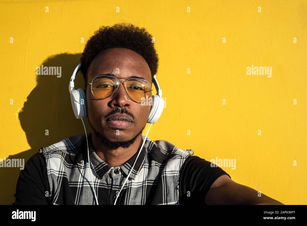 Portrait of young man listening music with headphones against yellow wall Stock Photo