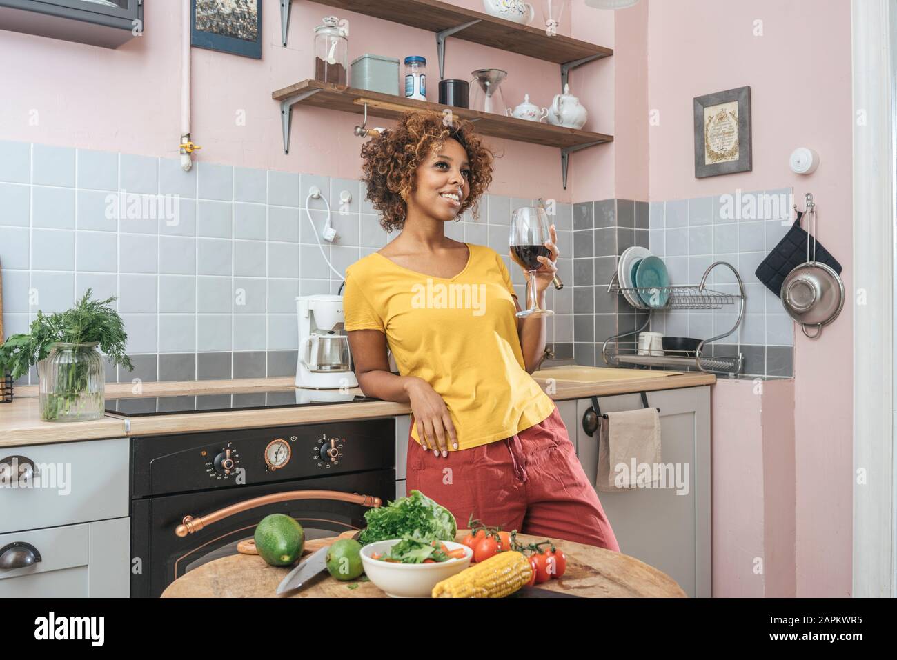 Smiling young woman drinking glass of red wine in kitchen Stock Photo