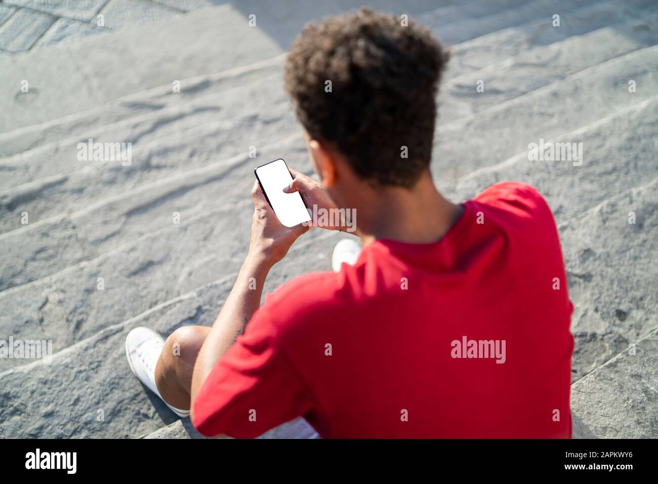 Young man sitting on outdoor stairs checking his smartphone Stock Photo ...