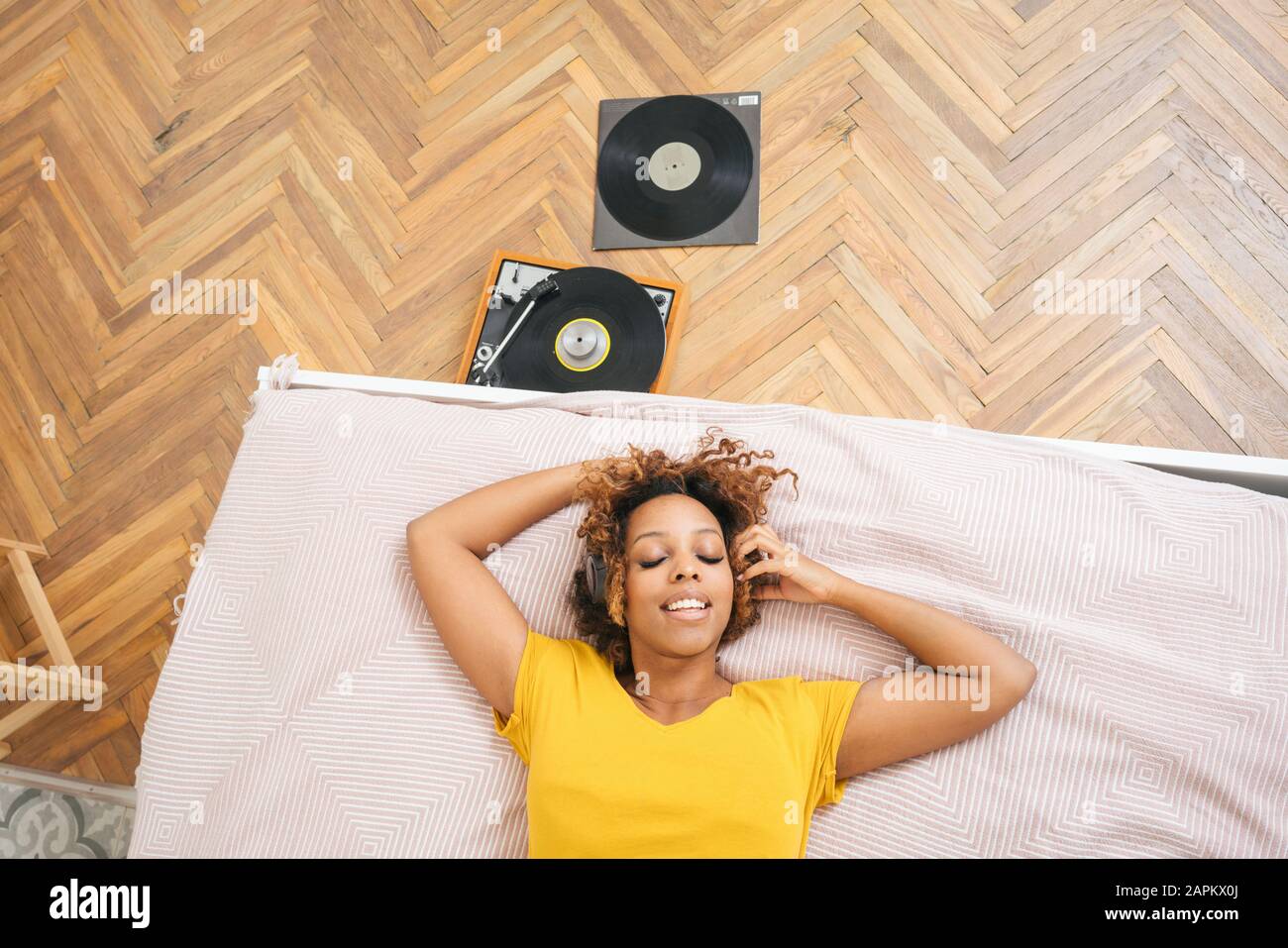 Young woman lying on bed listening to music with headphones and record player Stock Photo