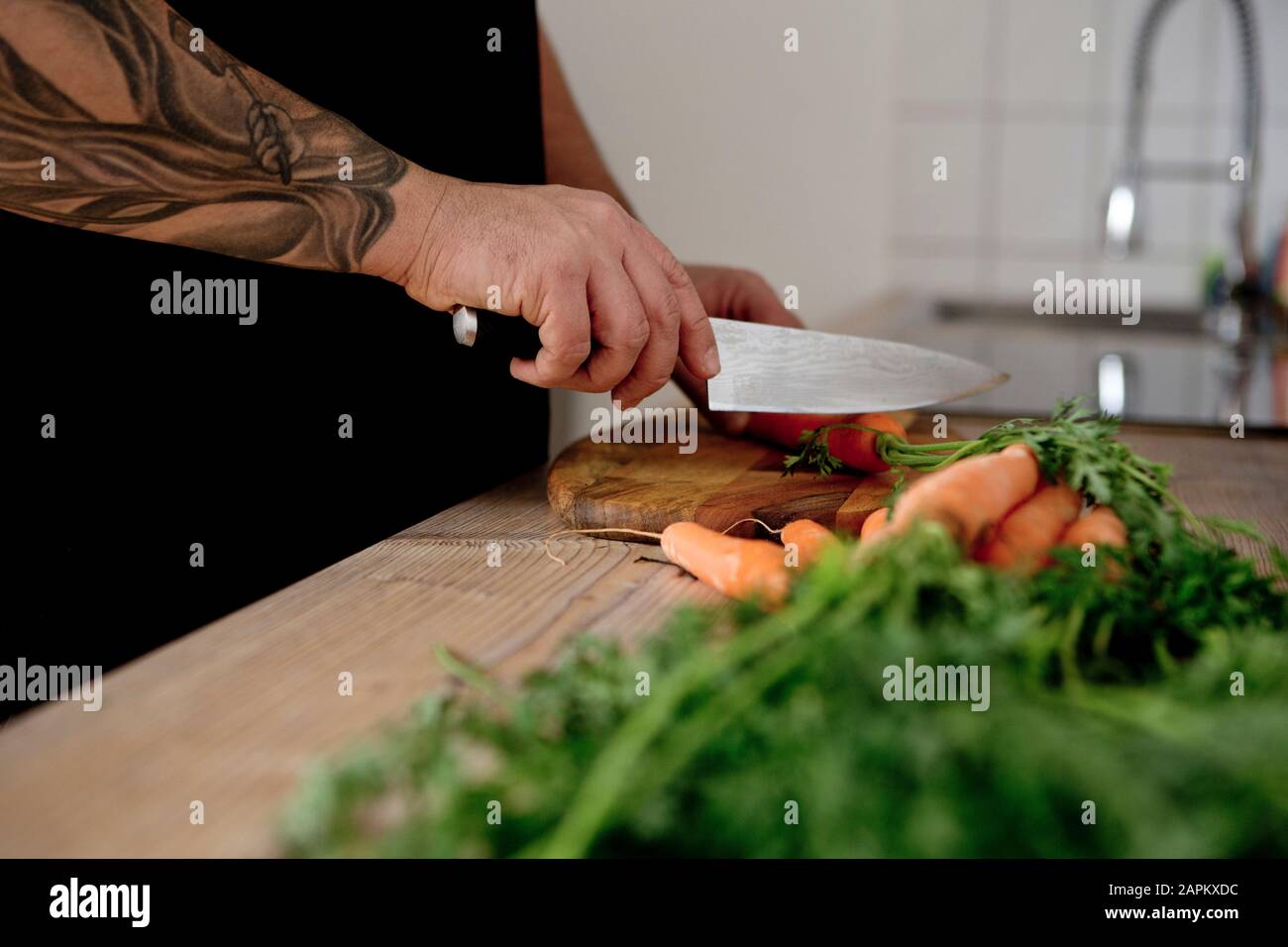 Close-up of tattooed man custting carrots in kitchen Stock Photo