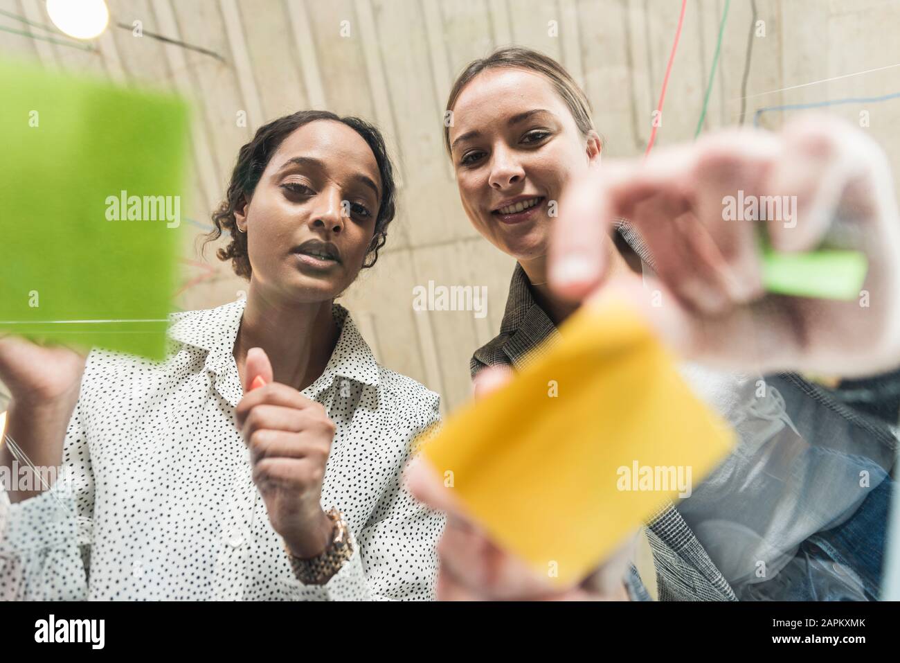 Two young businesswomen working on adhesive notes on glass table Stock Photo
