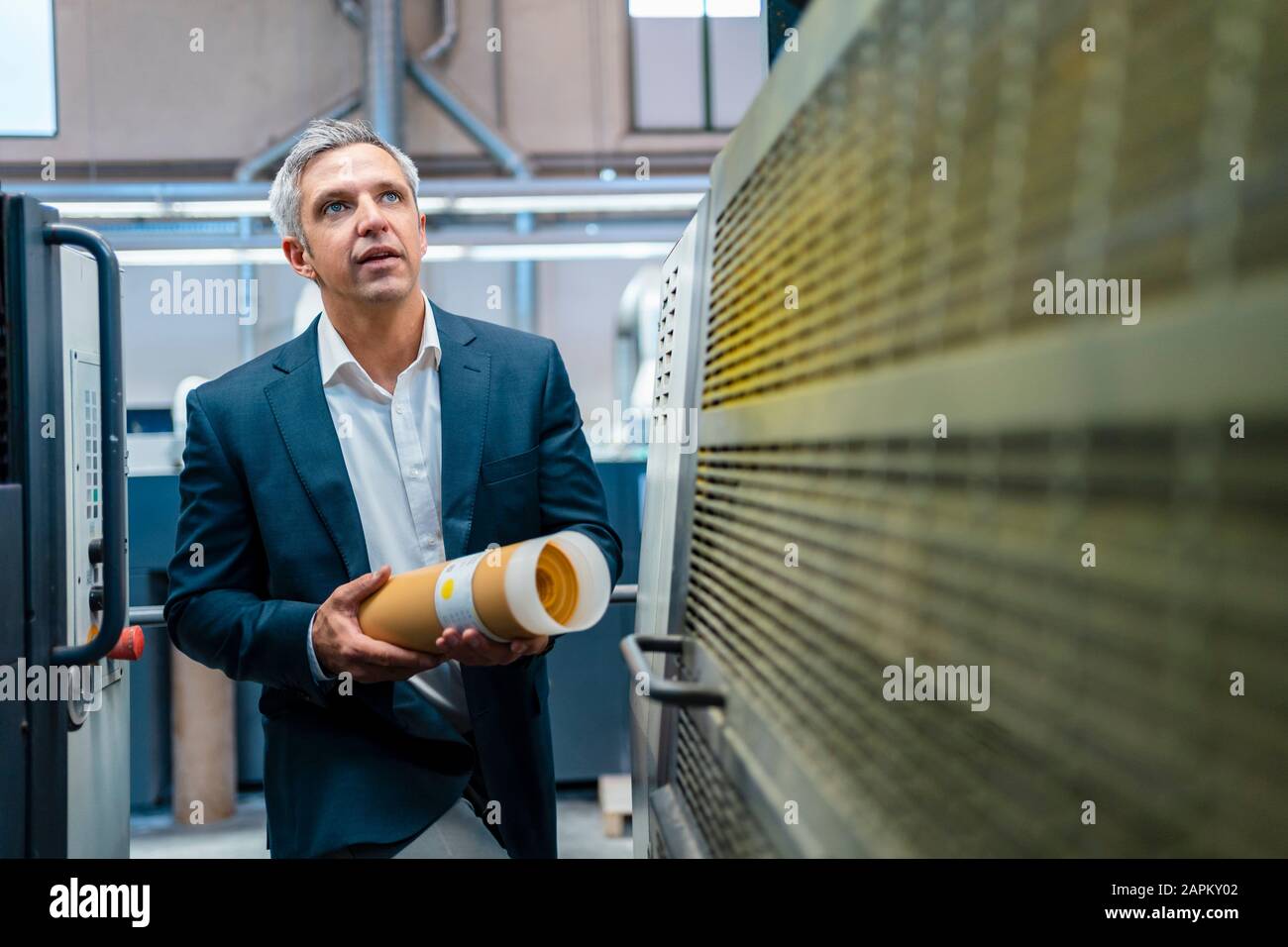 Businessman in a factory looking at a machine Stock Photo