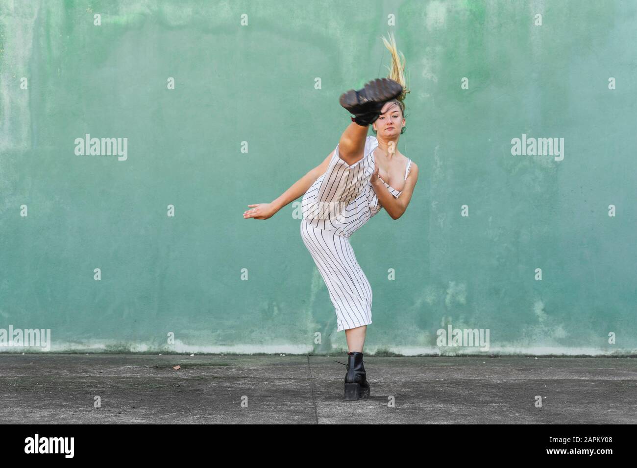 Young woman doing a high kick in front of green wall Stock Photo