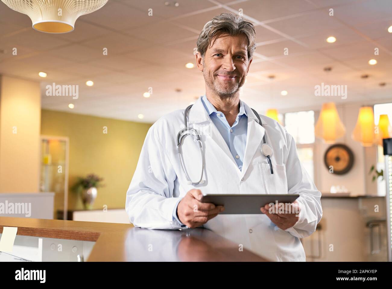 Portrait of confident doctor with tablet at reception in his medical practice Stock Photo