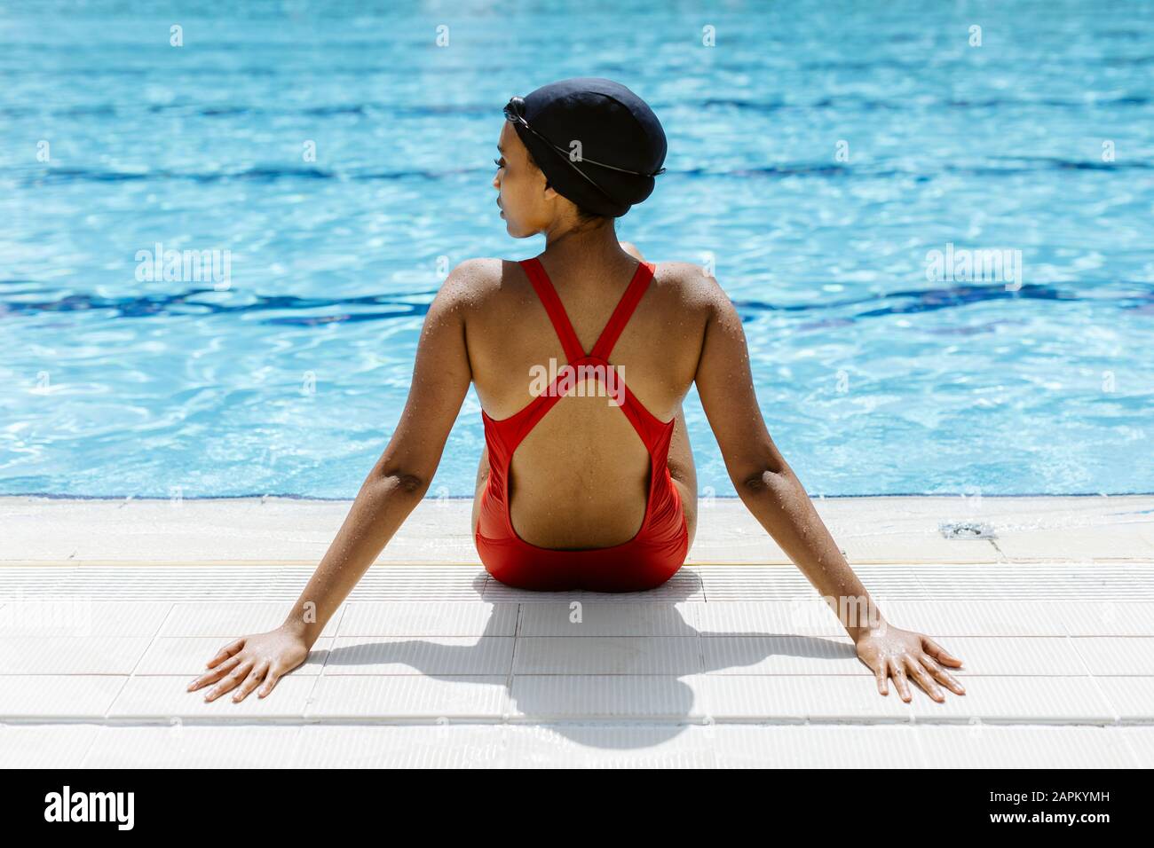 Back view of young woman wearing red swimsuit and swimming cap relaxing ...