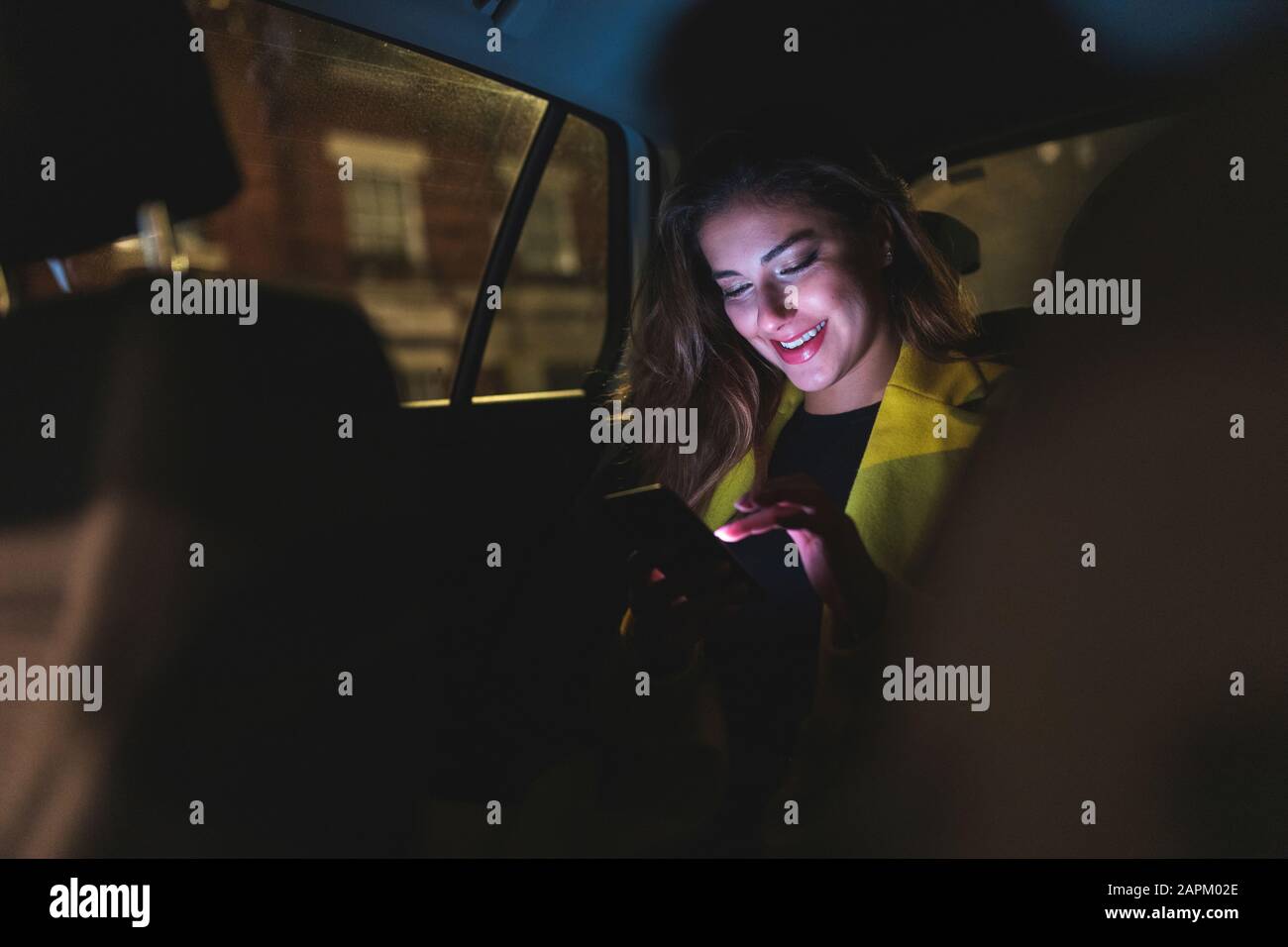 Woman sitting on the backseat of a car in the city at night Stock Photo
