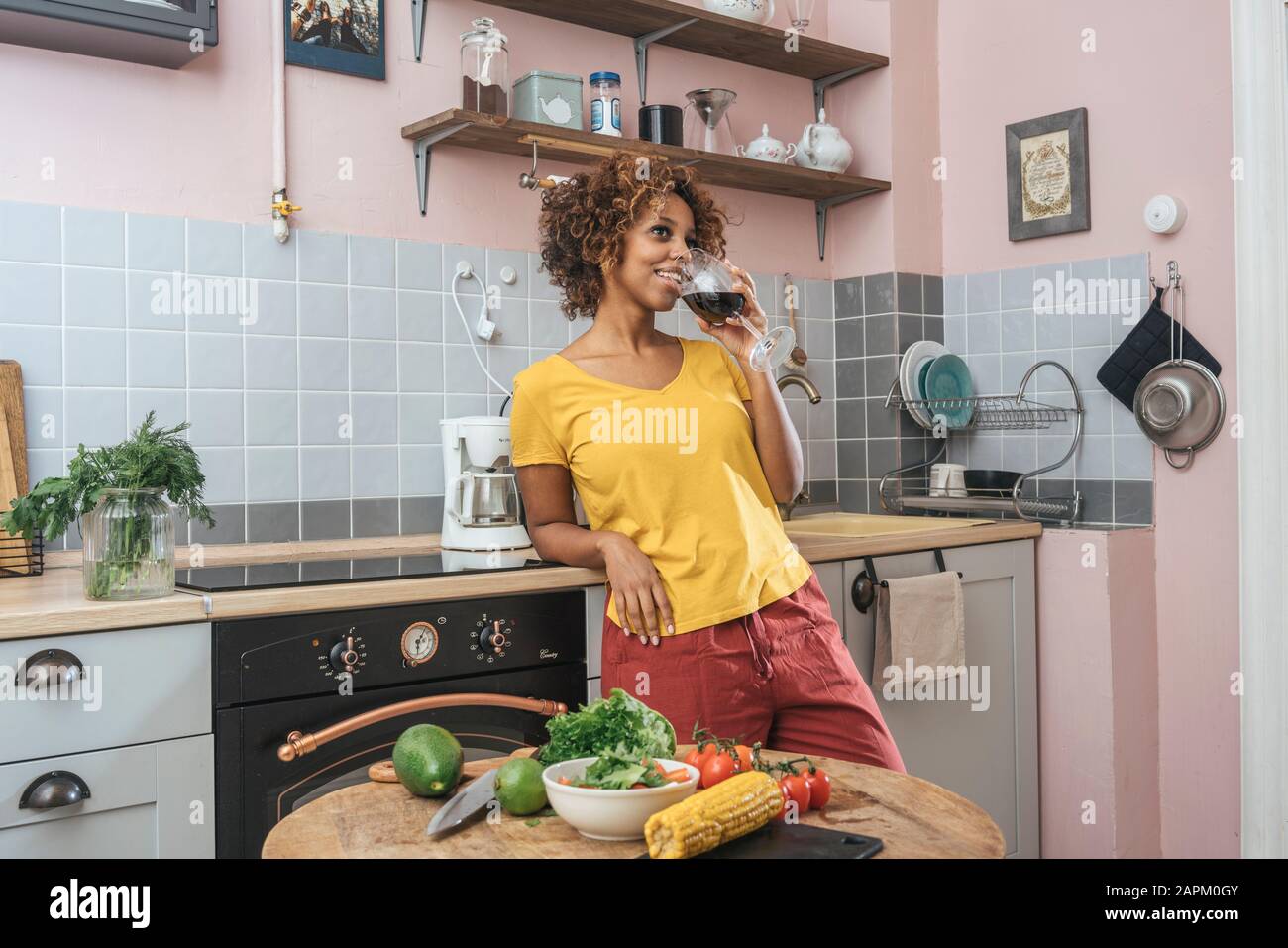 Smiling young woman drinking glass of red wine in kitchen Stock Photo