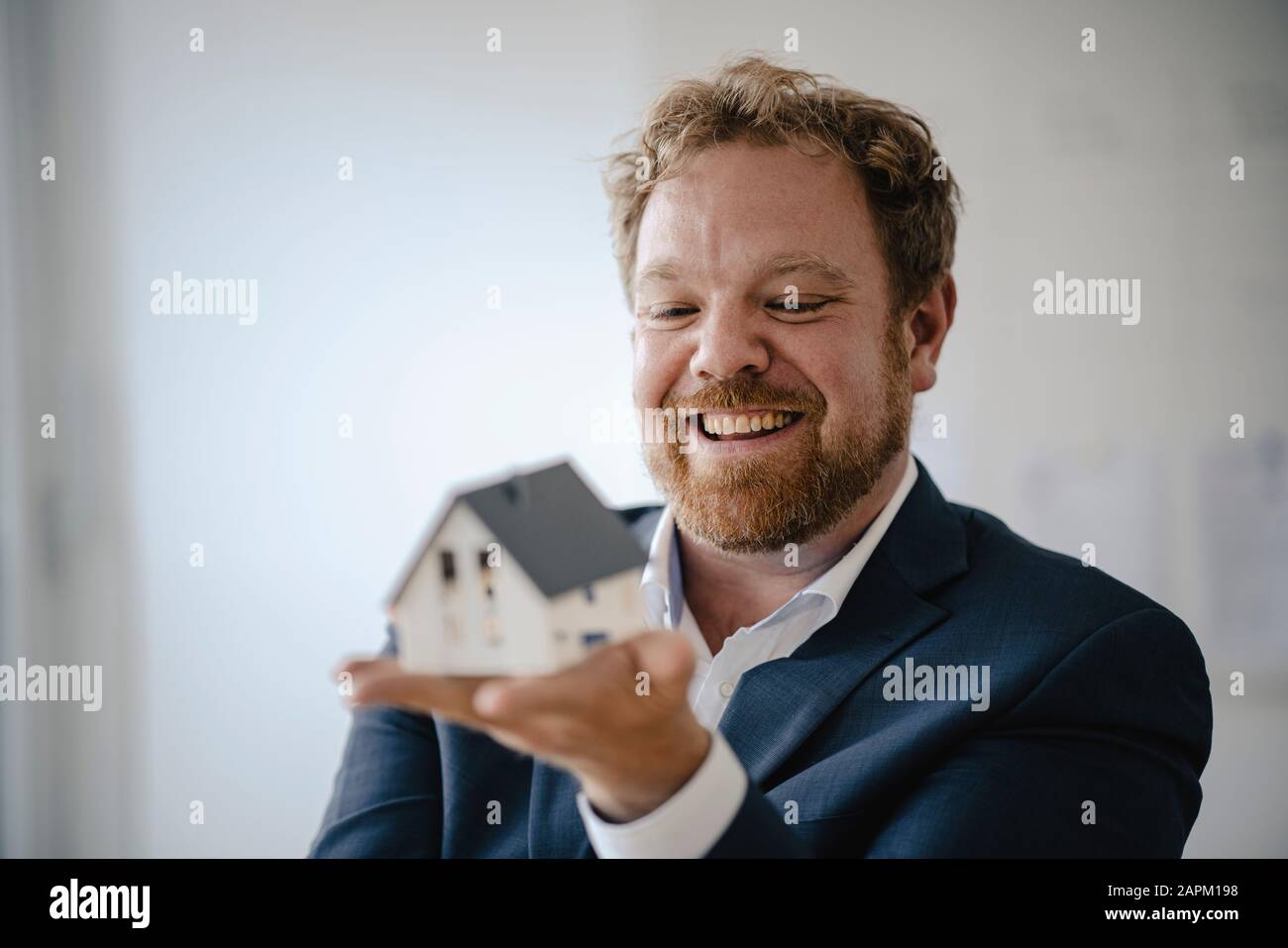 Happy businessman holding model house in office Stock Photo