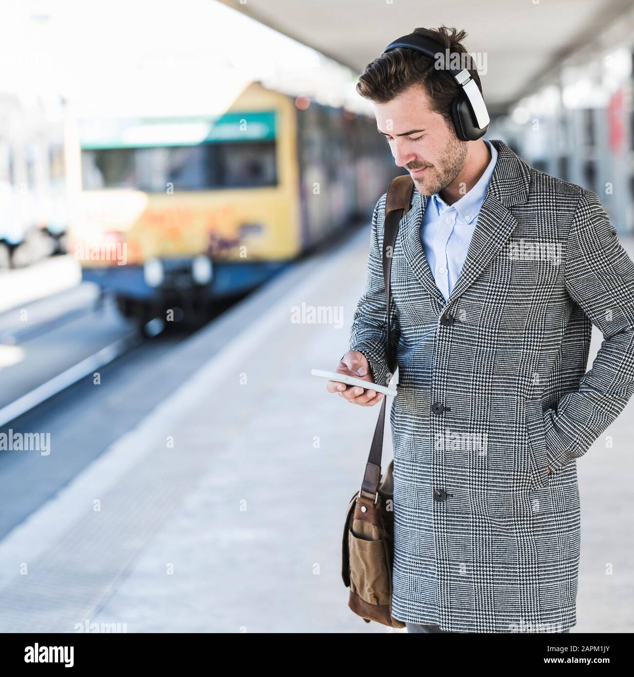 Young businessman with cell phone and headphones at the train station Stock Photo