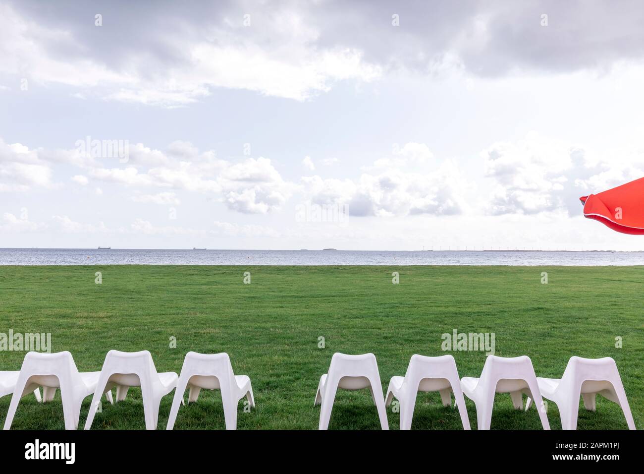Denmark, Charlottenlund, White empty chairs on green lawn with Oresund strait in background Stock Photo
