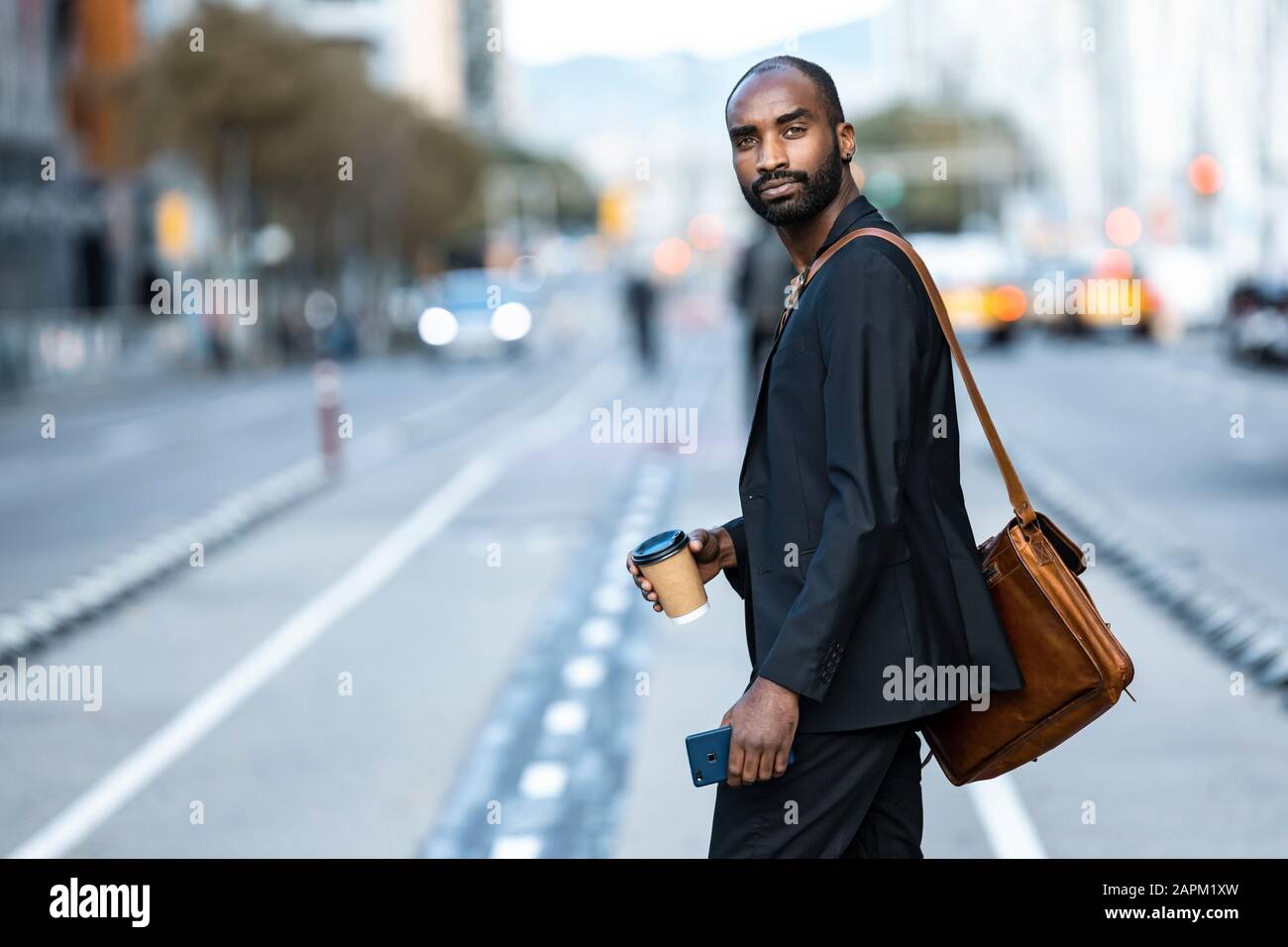 Portrait of young businessman with coffee to go crossing the street ...