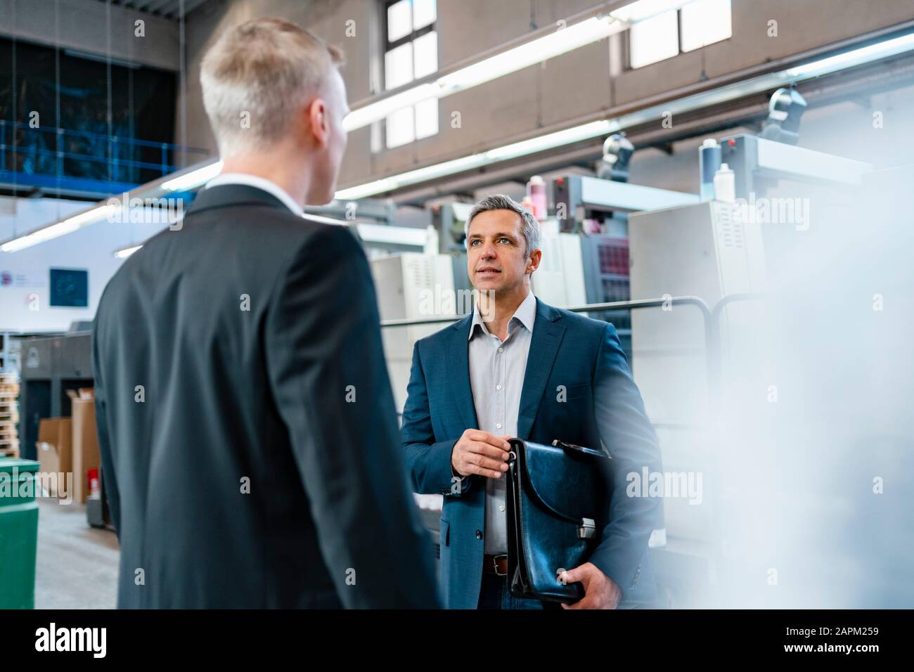 Two businessmen talking in a factory Stock Photo - Alamy