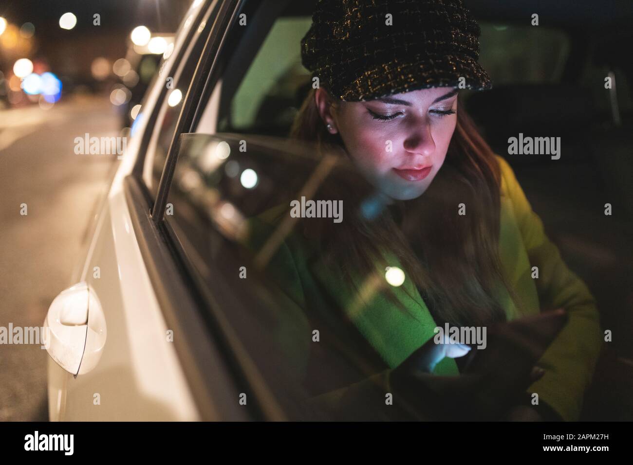 Woman sitting on the backseat of a car in the city at night Stock Photo